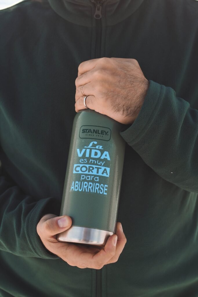 A man holding a green insulated water bottle with Spanish text and a casual outfit.